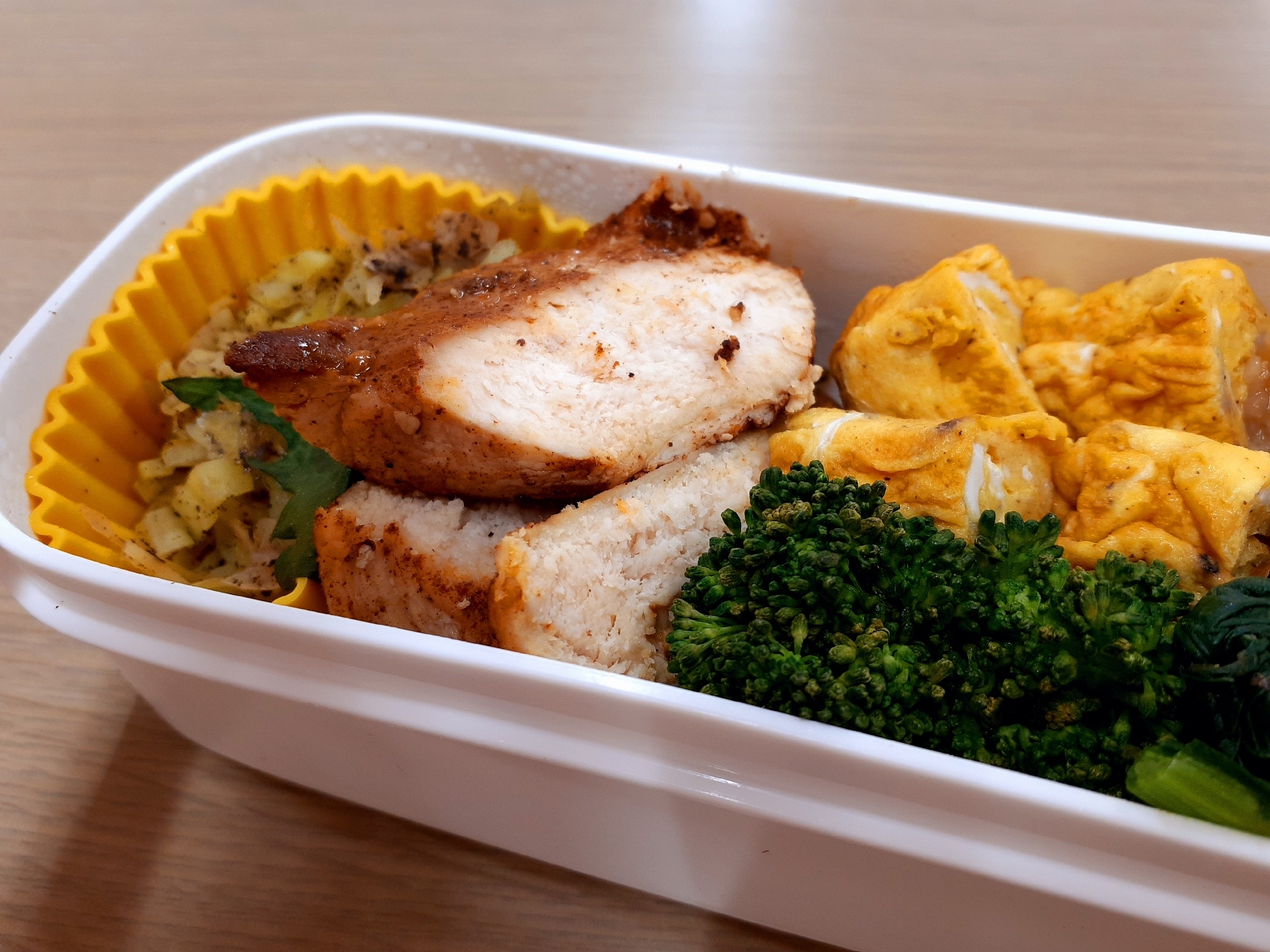 白い弁当箱に入ったケイジャンチキンと卵焼きやブロッコリー
