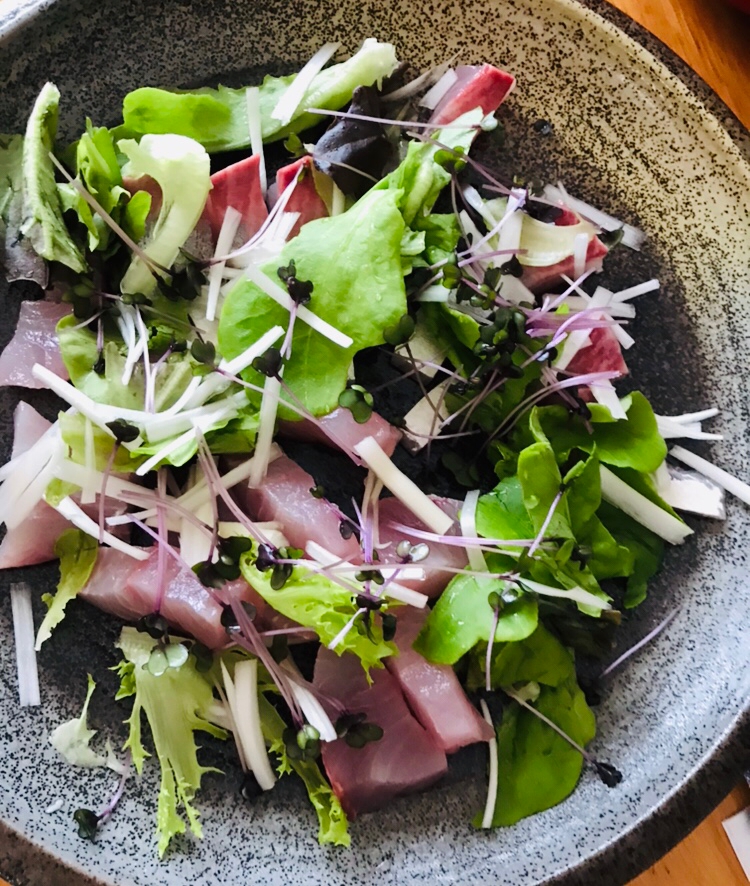 黒の陶器の皿に盛りつけられたヒラマサとサラダ菜の中華風サラダ