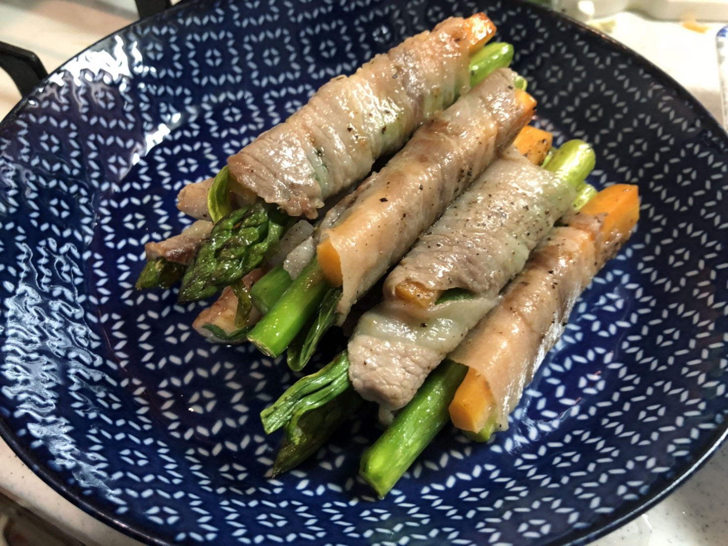 模様入りの紺色の皿に盛られた行者にんにく豚肉巻き