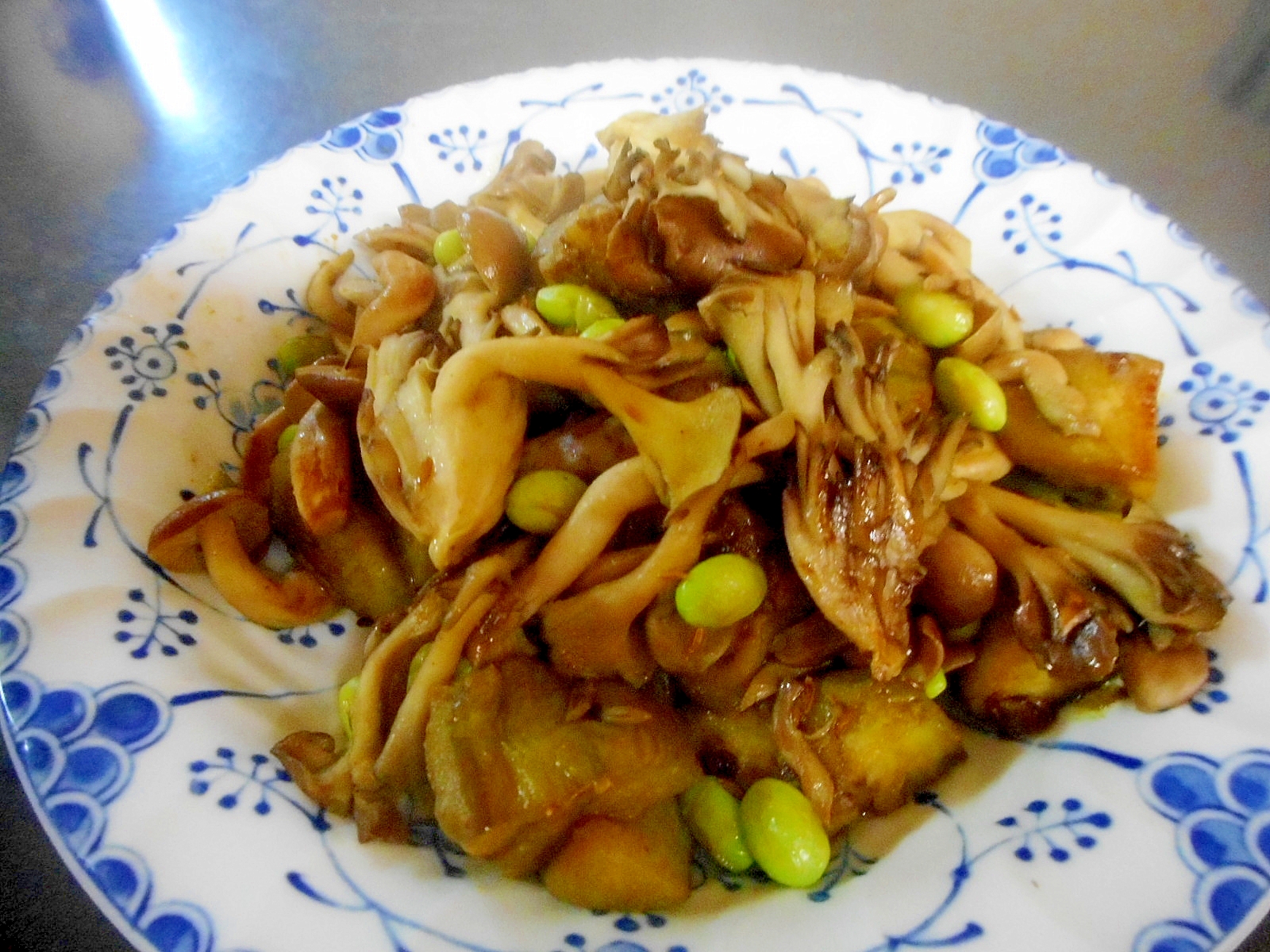 青い絵柄の皿に入った白なすと舞茸と枝豆のバター蒸し
