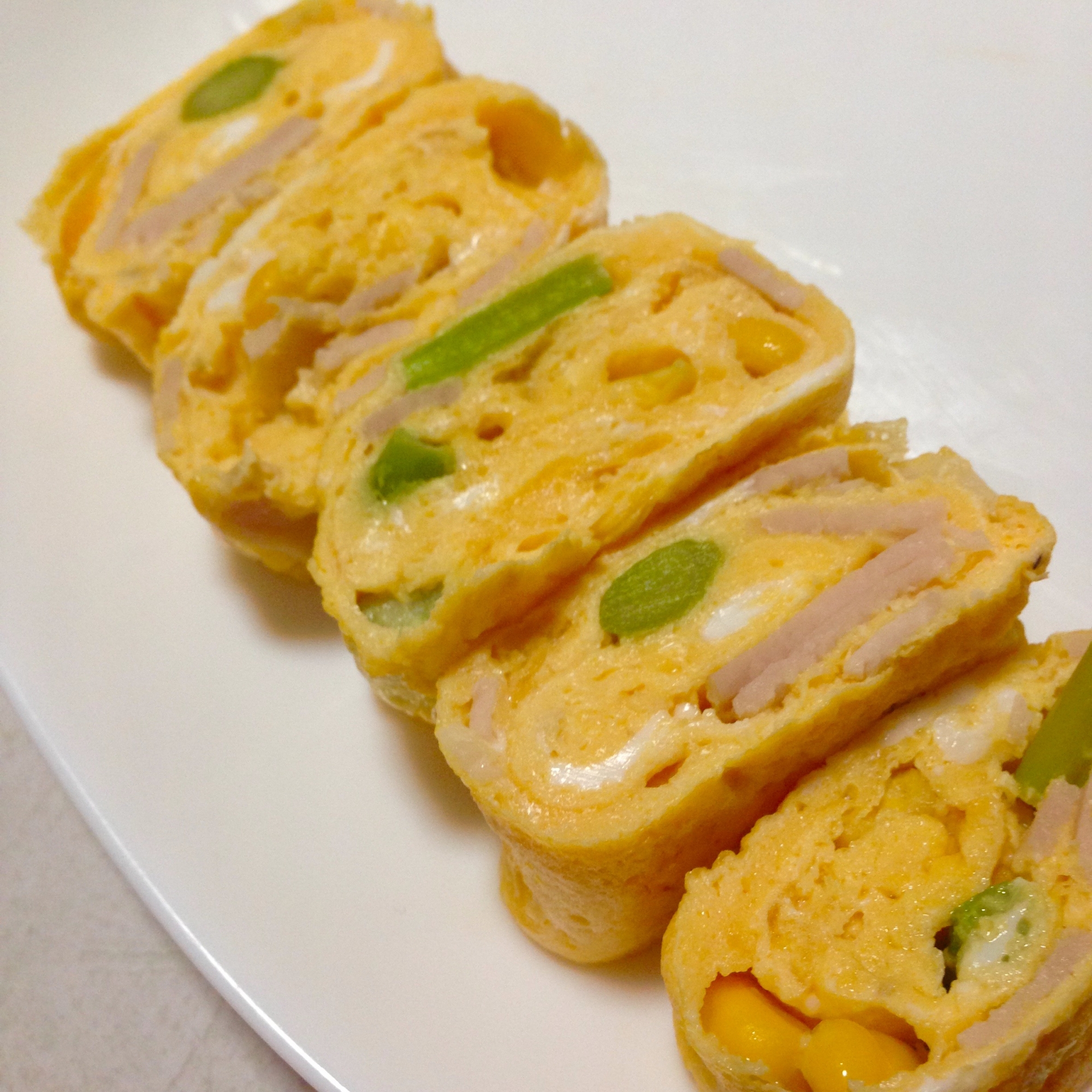 白色の皿に盛られた冷凍アスパラ、コーン、ハムの卵焼き