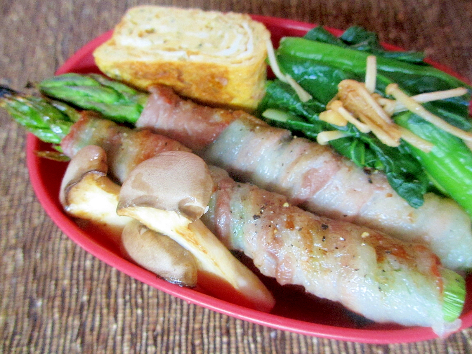 赤い弁当箱に盛られたアスパラガスのウイスキー豚バラ肉巻き