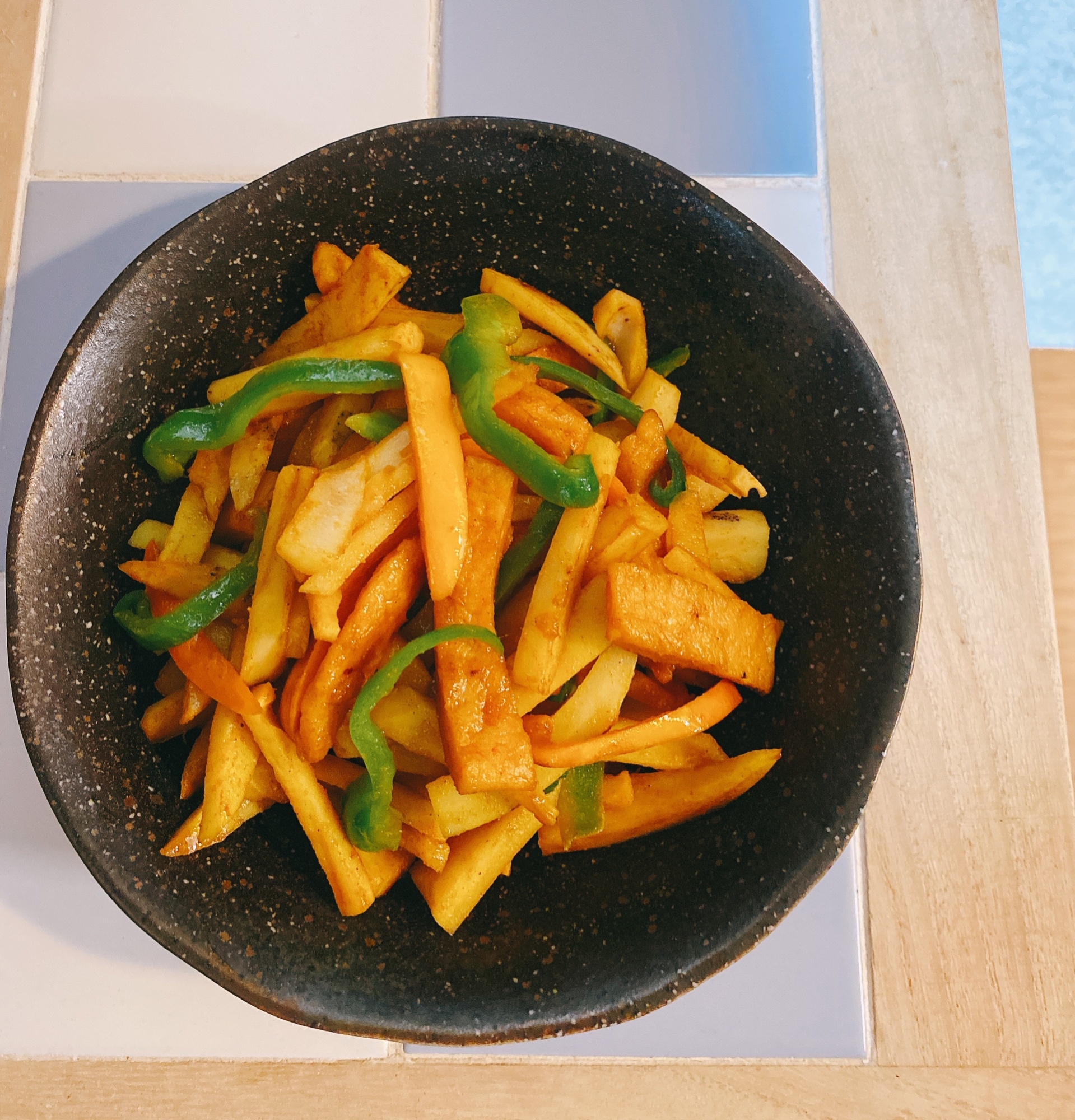 黒い皿に盛り付けられたれんこんとピーマンのカレー風味炒め