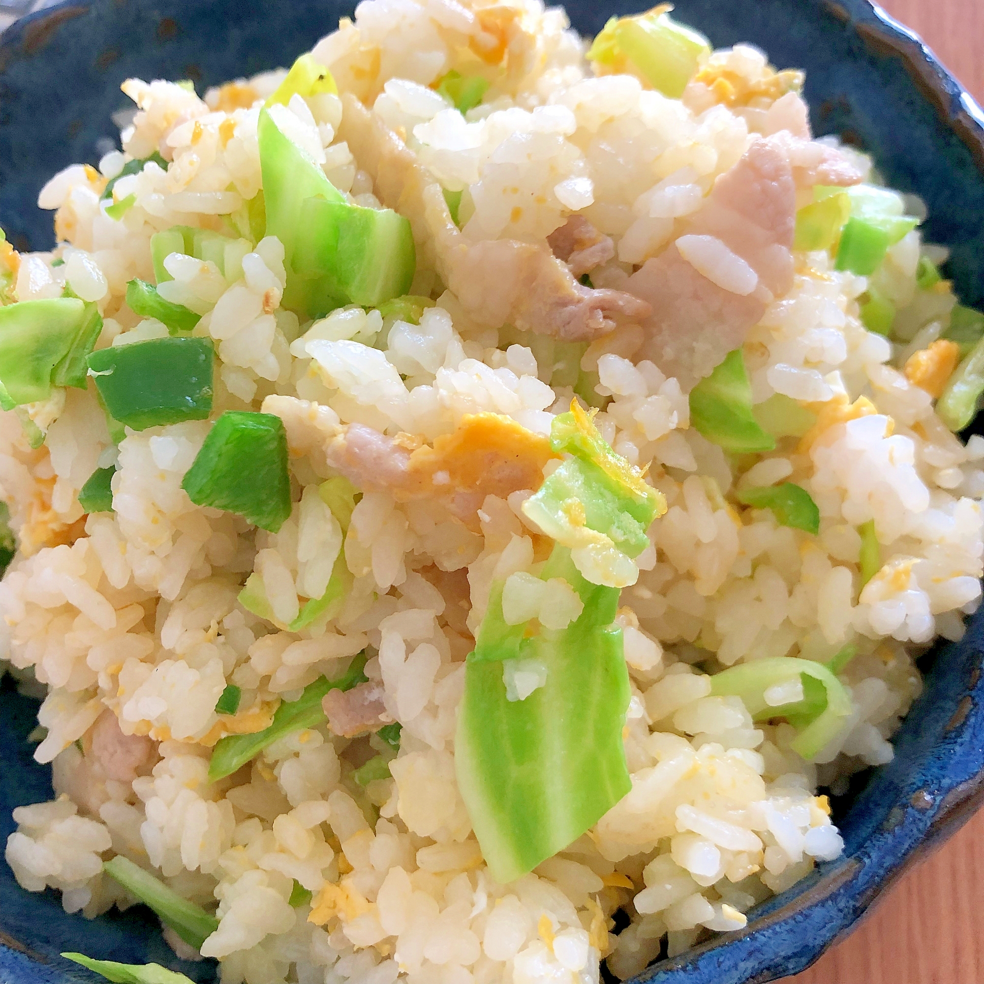 青い皿に盛り付けた豚肉とキャベツの卵チャーハン