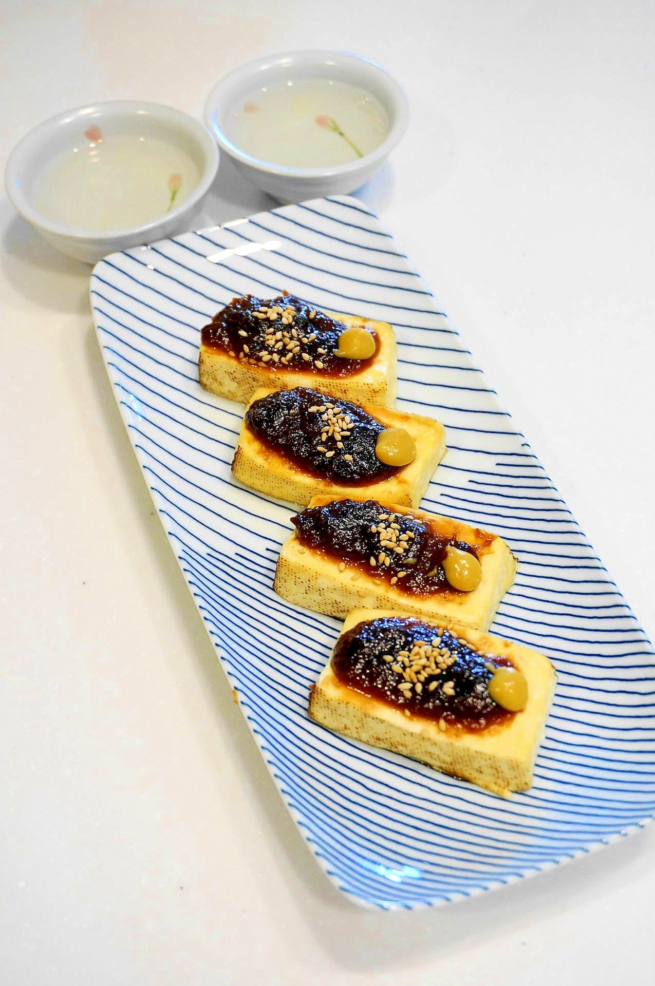 青い線が入った白い角皿に盛り付けられた焼き豆腐の赤味噌田楽