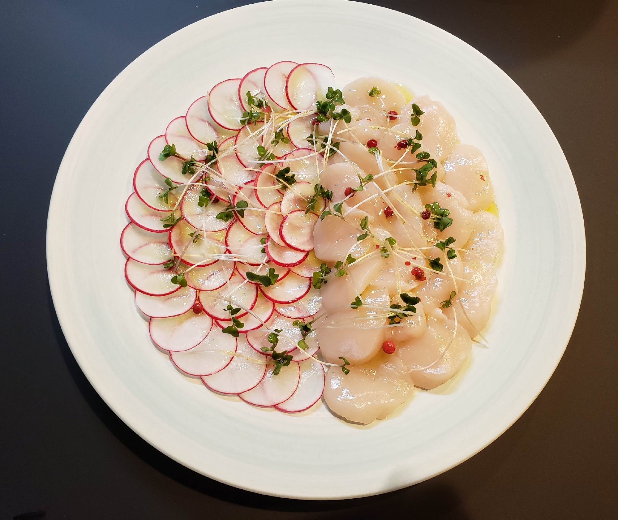 ホタテとラディッシュのカルパッチョが白い皿に盛り付けられているところ