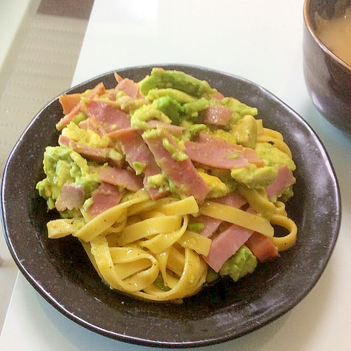 黒い皿に盛られた、アボカドとベーコンのパスタ