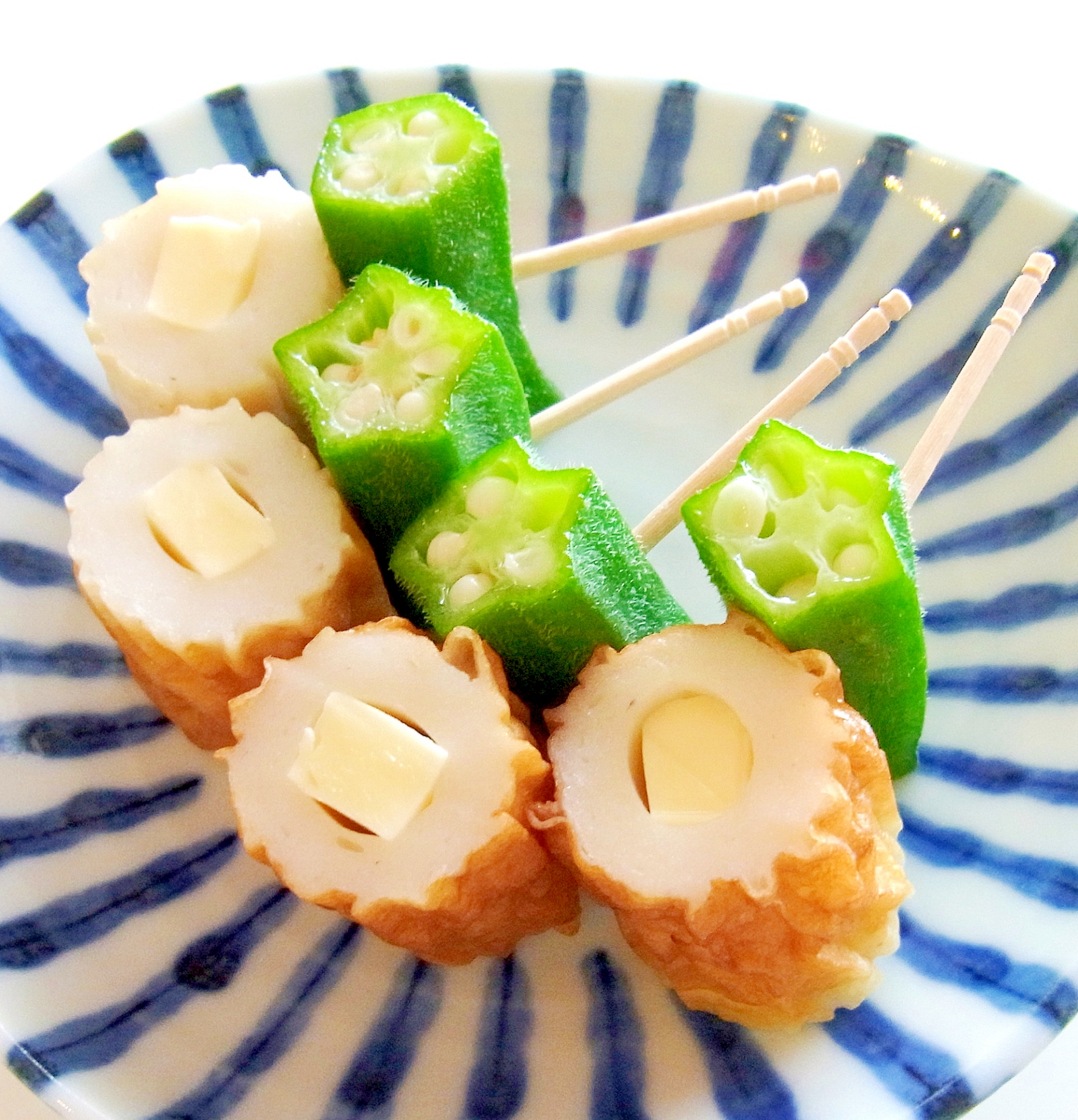 青色の縞模様の皿に盛られたチーズちくわとオクラの串