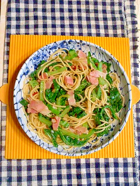 青い柄が入った白い皿に盛り付けられたかつお菜とベーコンのペペロンチーノパスタ