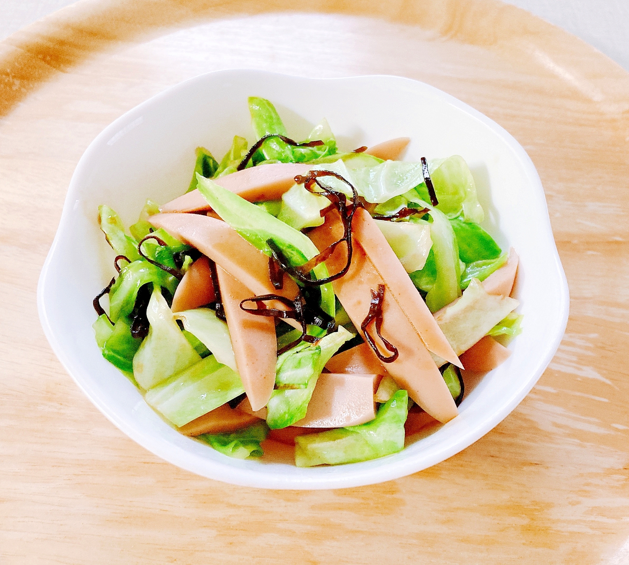 白いお皿に盛り付けられたキャベツと魚肉ソーセージの塩昆布炒め