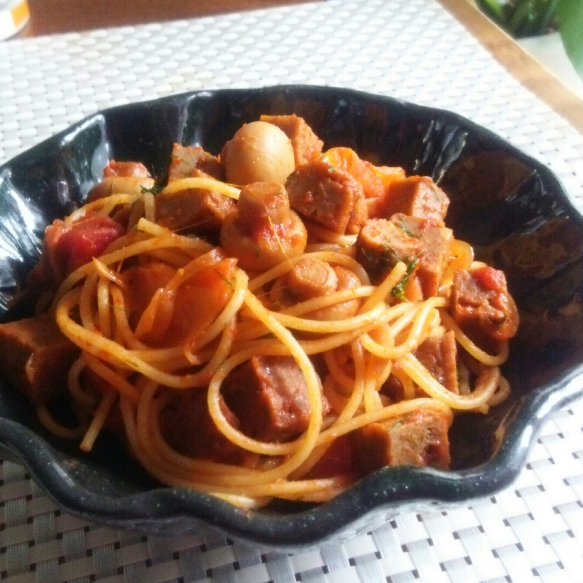 黒い皿に盛られたマルシンハンバーグのトマトソースパスタ