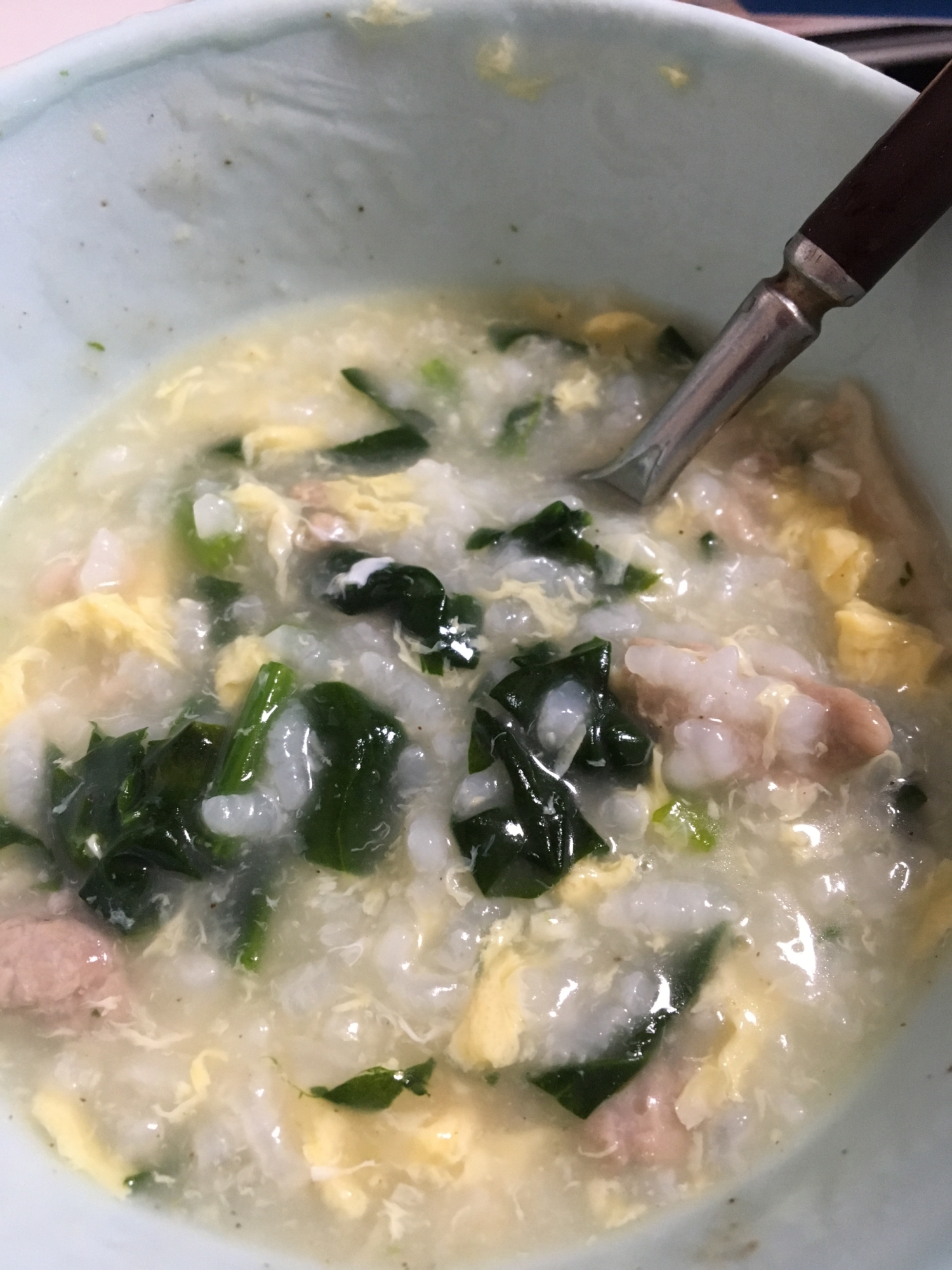 白い器に盛られた豚肉とほうれん草の中華がゆ