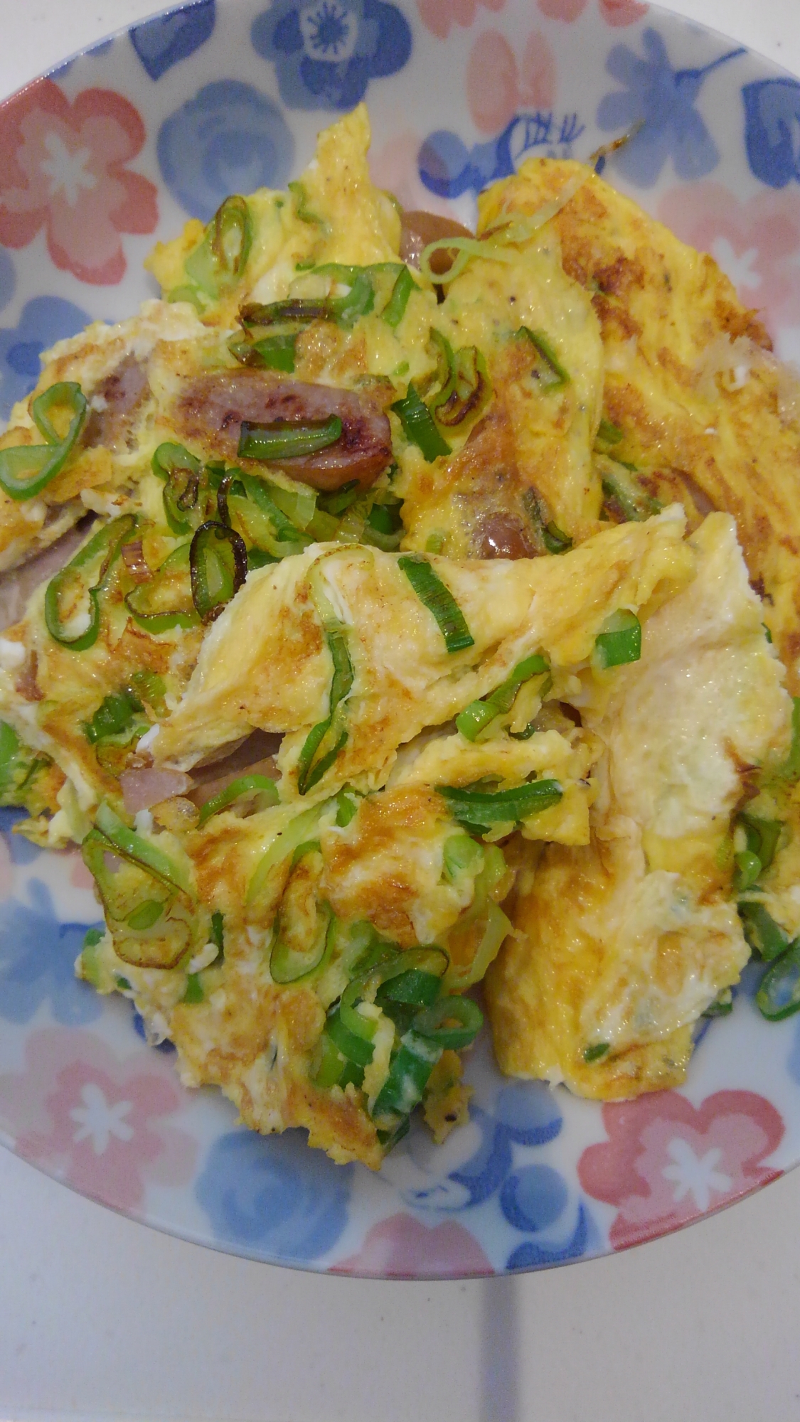 花柄の皿に盛られたウインナーソーセージと青ネギの卵炒め