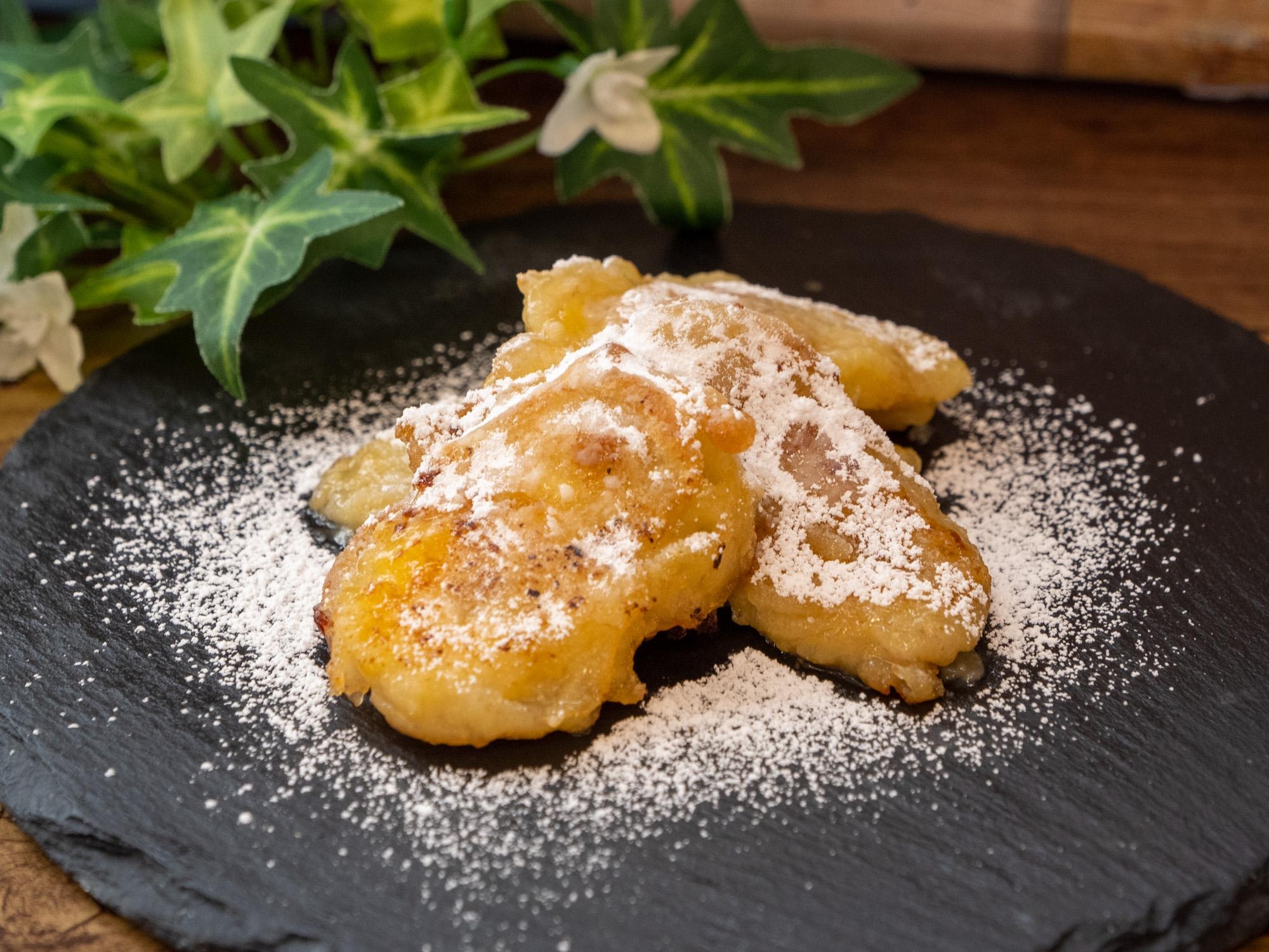 黒い皿にのせた粉砂糖をふったバナナの天ぷら