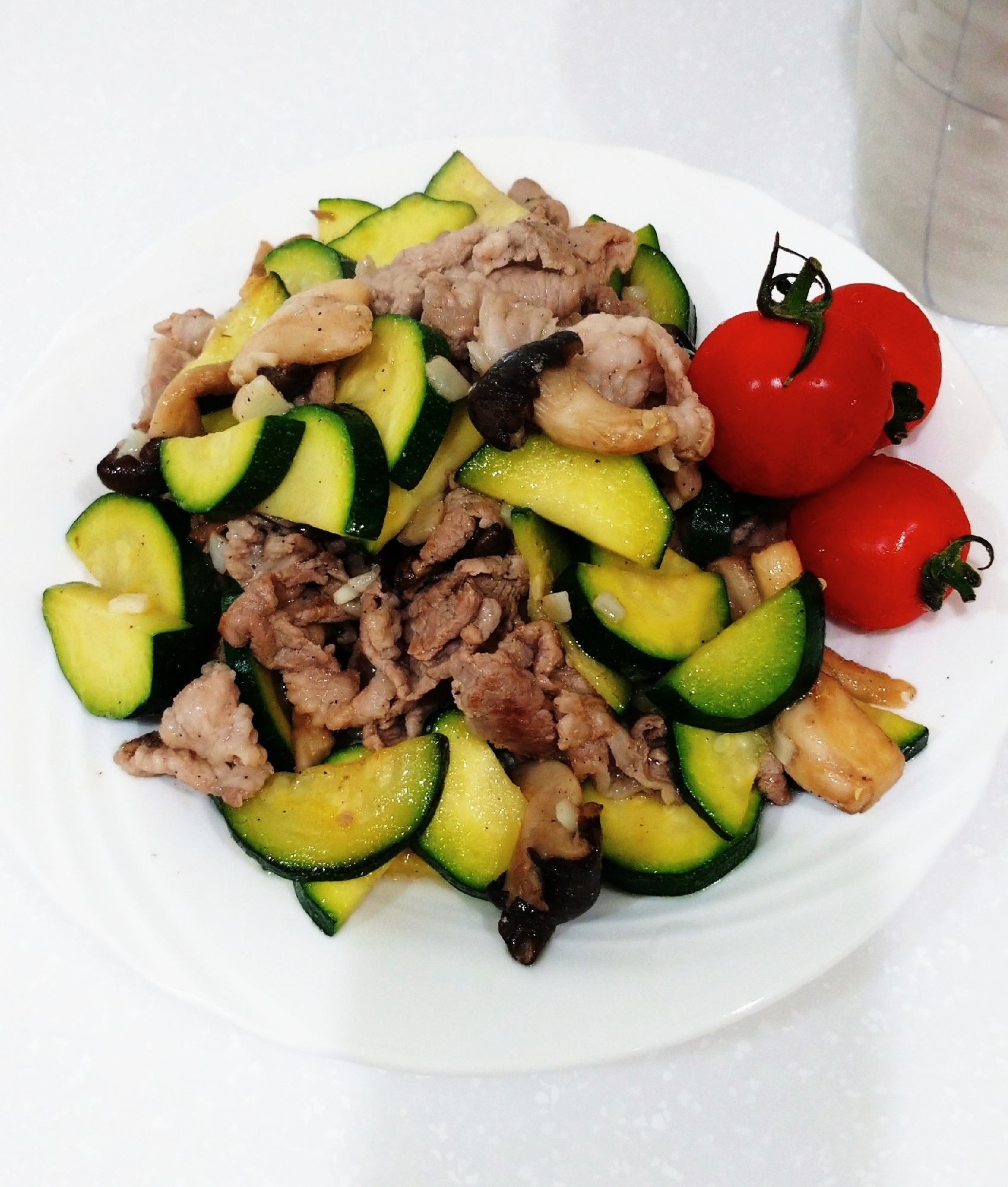 白色の丸皿に盛られた豚肉とズッキーニとヒラタケの塩こしょうにんにく炒め