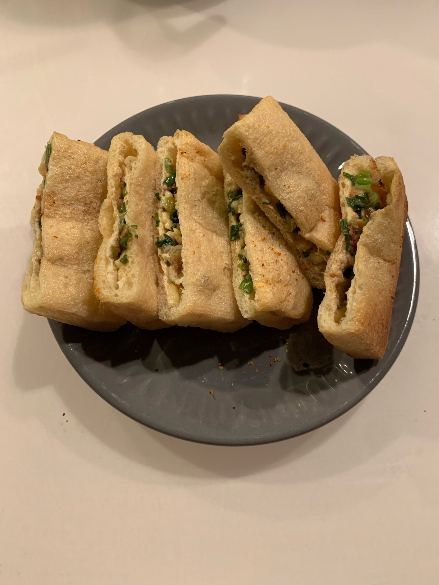 黒い皿に盛られた油揚げと青ネギのチーズ焼き