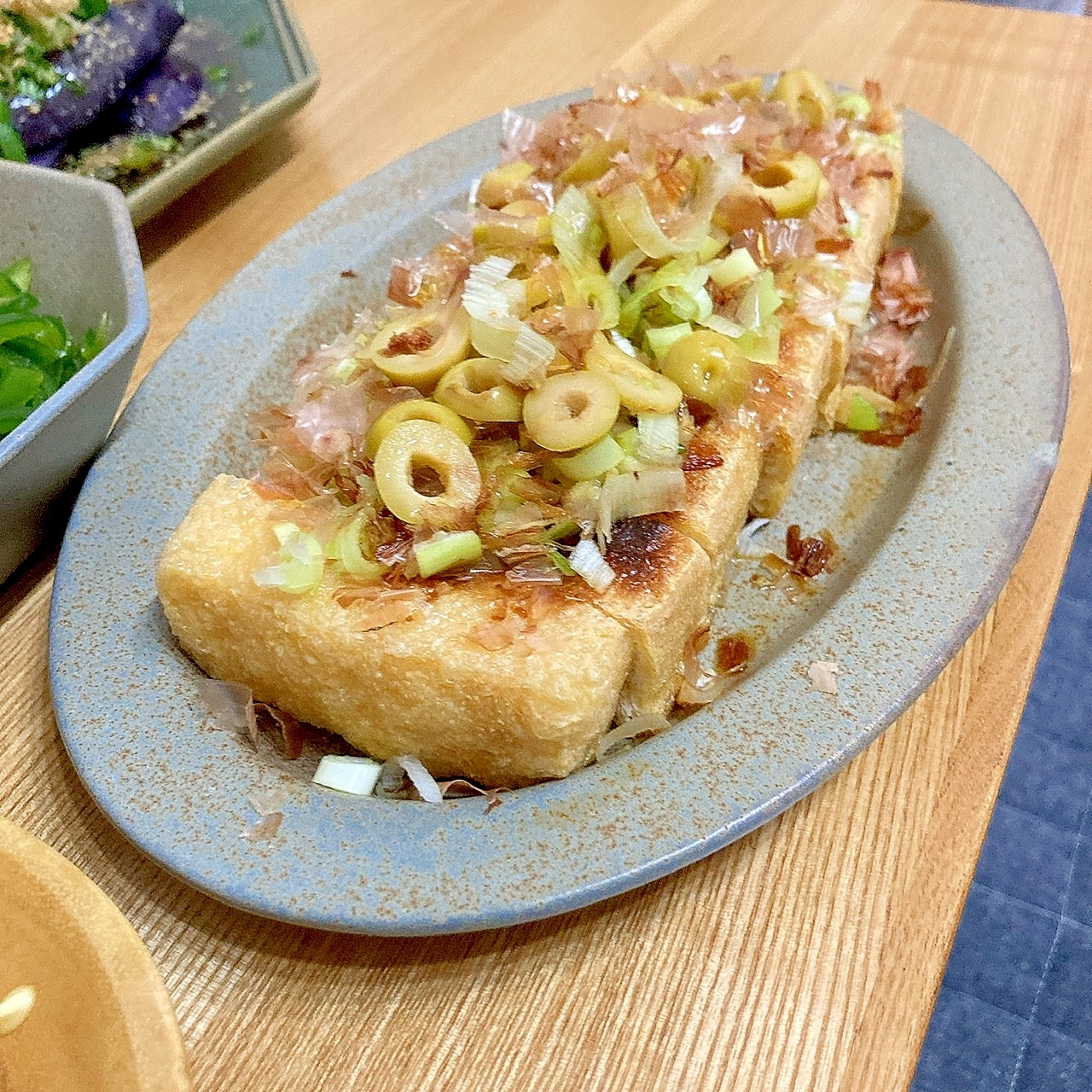 グレーの皿に盛り付けた焼き栃尾揚げのオリーブのせ