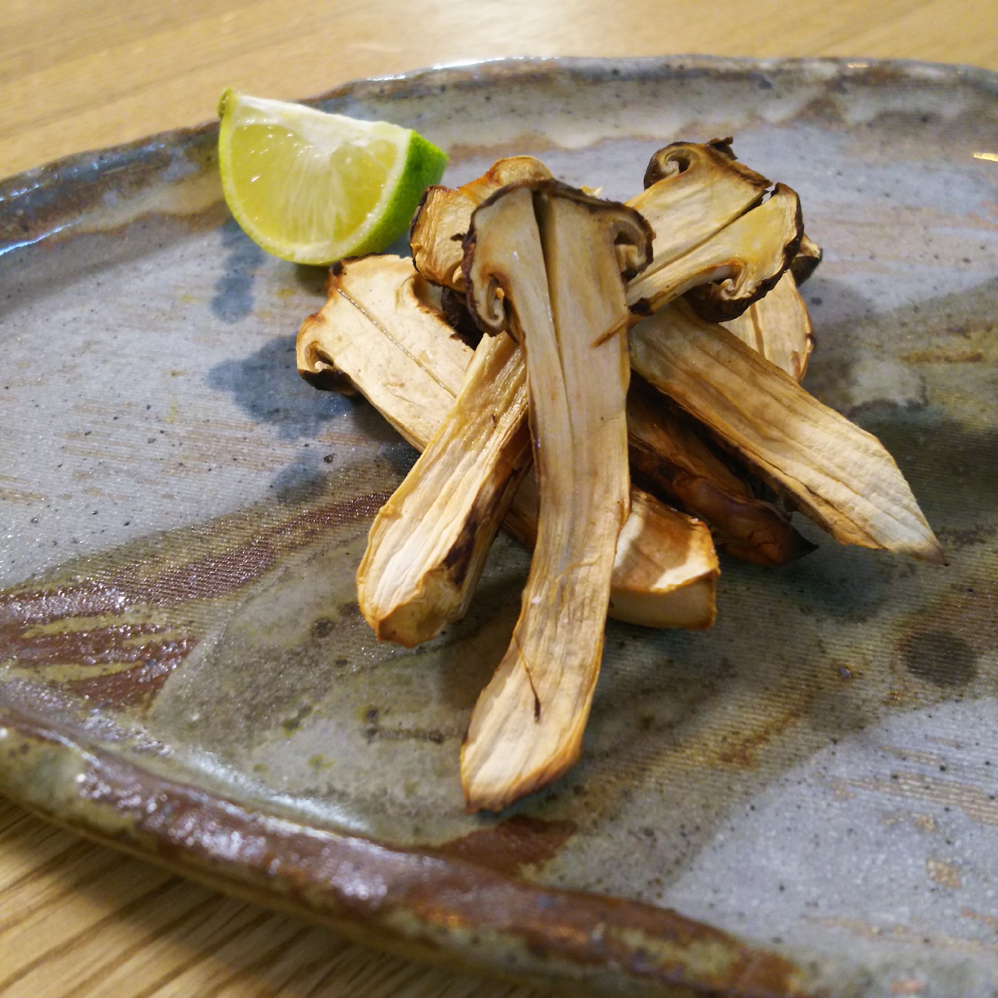 グレーの皿に焼き松茸とすだちが盛り付けられている