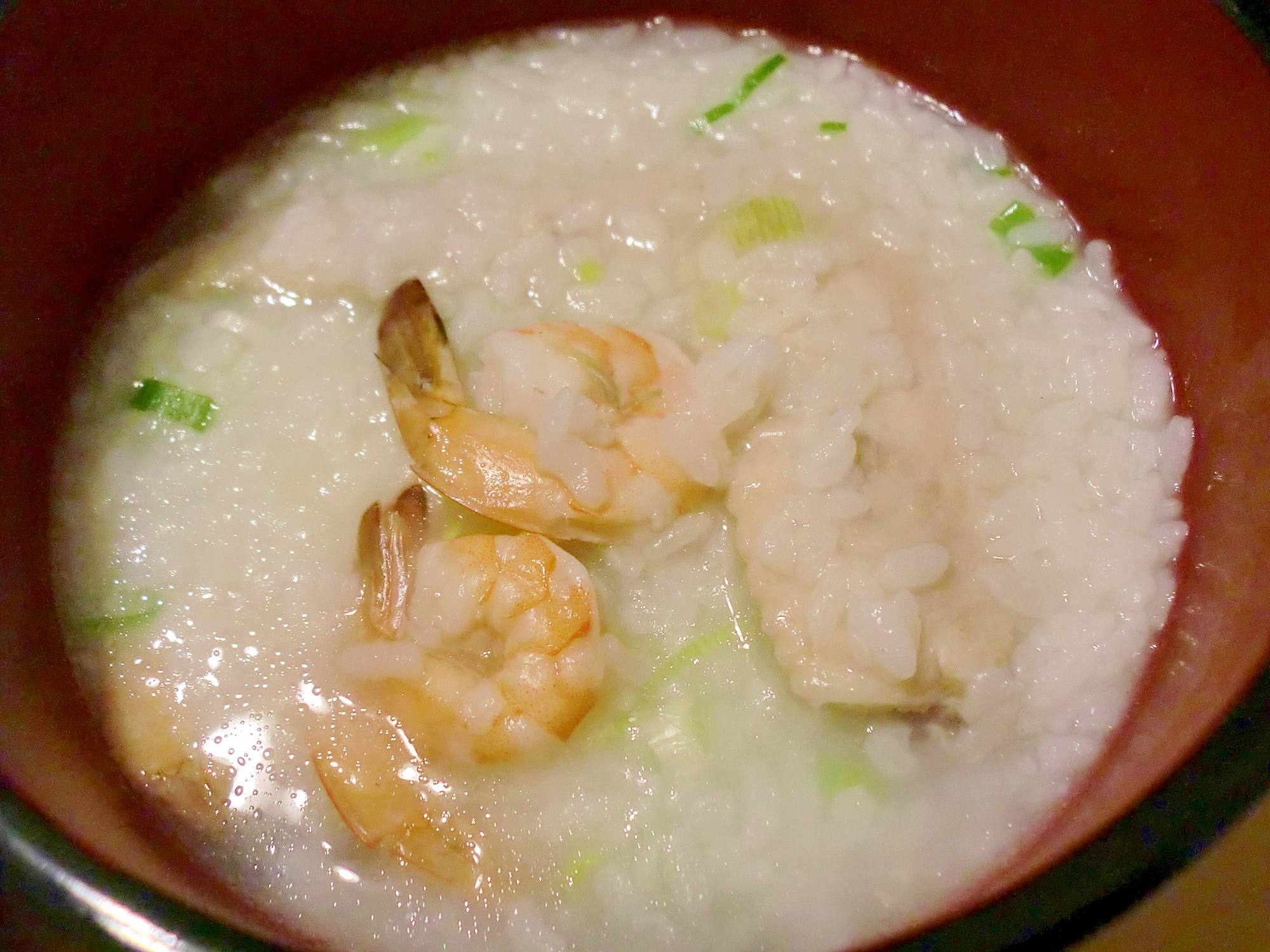 茶色い器に盛られたむきえびと鶏手羽先の中華がゆ